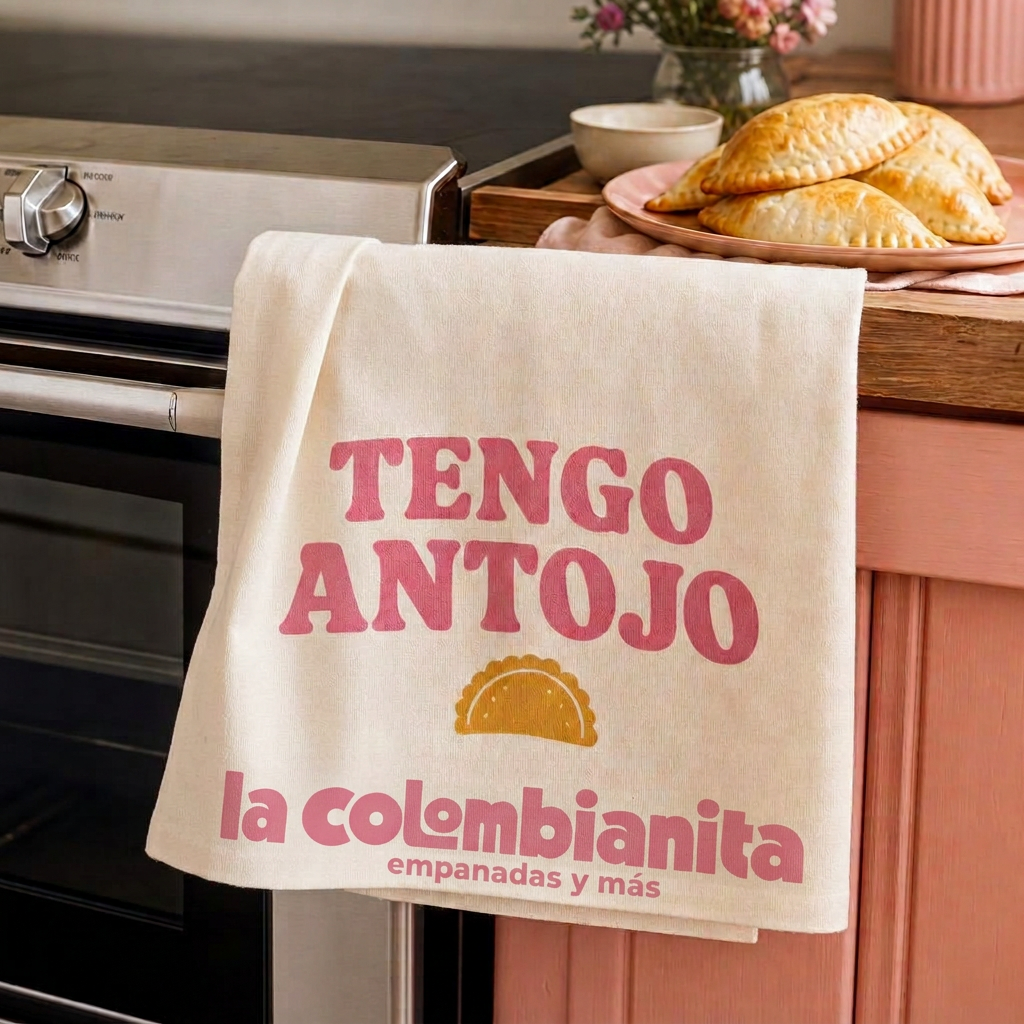 Crèmekleurige theedoek met TENGO ANTOJO over een ovendeur in een keuken